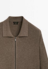 Cardigan marron en maille côtelée avec fermeture éclair et col replié, présenté à plat sur un fond blanc.