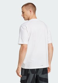 Hvid bomulds T-shirt med korte ærmer, rund hals og minimal branding på kanten, båret med mønstrede sorte og grå shorts.