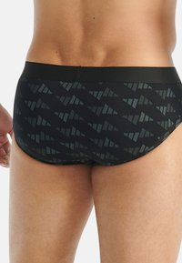 Czarne kąpielówki z geometrycznym wzorem w ciemnoszarym kolorze. Gładki materiał z miękkim pasem biodrowym. Widok z tyłu pokazuje dopasowanie i szczegóły designu.