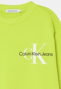 Felpa verde lime con scollo a girocollo a coste e tessuto strutturato. Presenta il logo "Calvin Klein Jeans" in bianco e marrone.