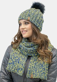 Cappello a maglia e sciarpa in blu e giallo con un motivo testurizzato; il cappello presenta un pompon nero; la sciarpa ha un design simile.