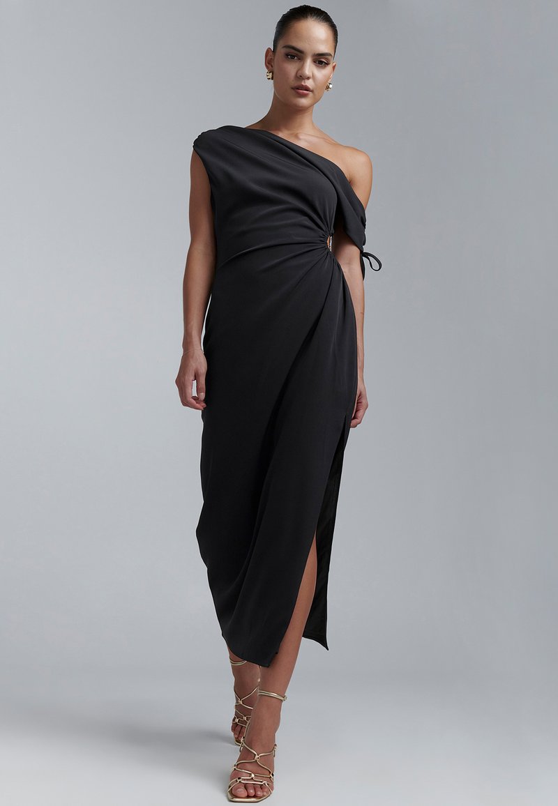 Juoda, viena peties suknelė, su drapiruota medžiaga, šonine skeltimi ir mazgo detale liemens srityje. Dėvima su aukso spalvos bateliais su dirželiais.