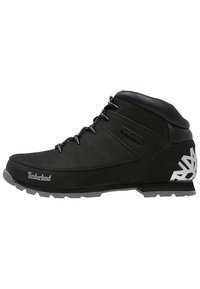 Botas de senderismo de cuero negro con un diseño de caña alta, puntera reforzada, suela texturizada y acentos geométricos blancos en el talón.