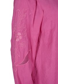 Tissu rose avec broderie florale et détail découpé en forme de treillis feuille sur une manche.