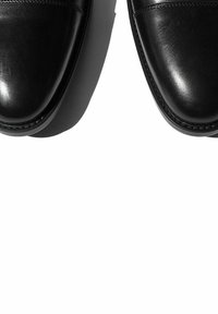Zapatos de vestir de cuero negro con un acabado liso, punteras redondeadas y costuras sutiles a lo largo de los bordes, con suela plana.
