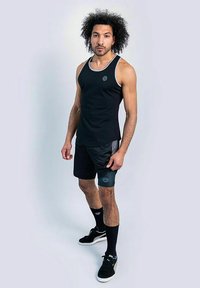 Canottiera nera senza maniche con scollatura grigia, abbinata a pantaloni corti neri con accenti grigi e logo, indossata con calze e scarpe nere.