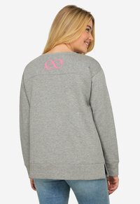Grå sweatshirt med avslappnad passform, med en broderad rosa oändlighetssymbol på baksidan och sidoöppningar vid fållen.