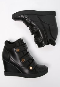 Svarta kilskor i läder med en slät yta, med en dragkedja, tre remmar och guldfärgad metall på framsidan.