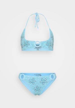 Jasnoniebieski strój kąpielowy składający się z biustonosza i majtek o błyszczącej teksturze. Halterneckowy stanik i majtki mają ozdoby w kształcie rozgwiazd. Zawiera również detal w postaci okrągłego pierścienia.