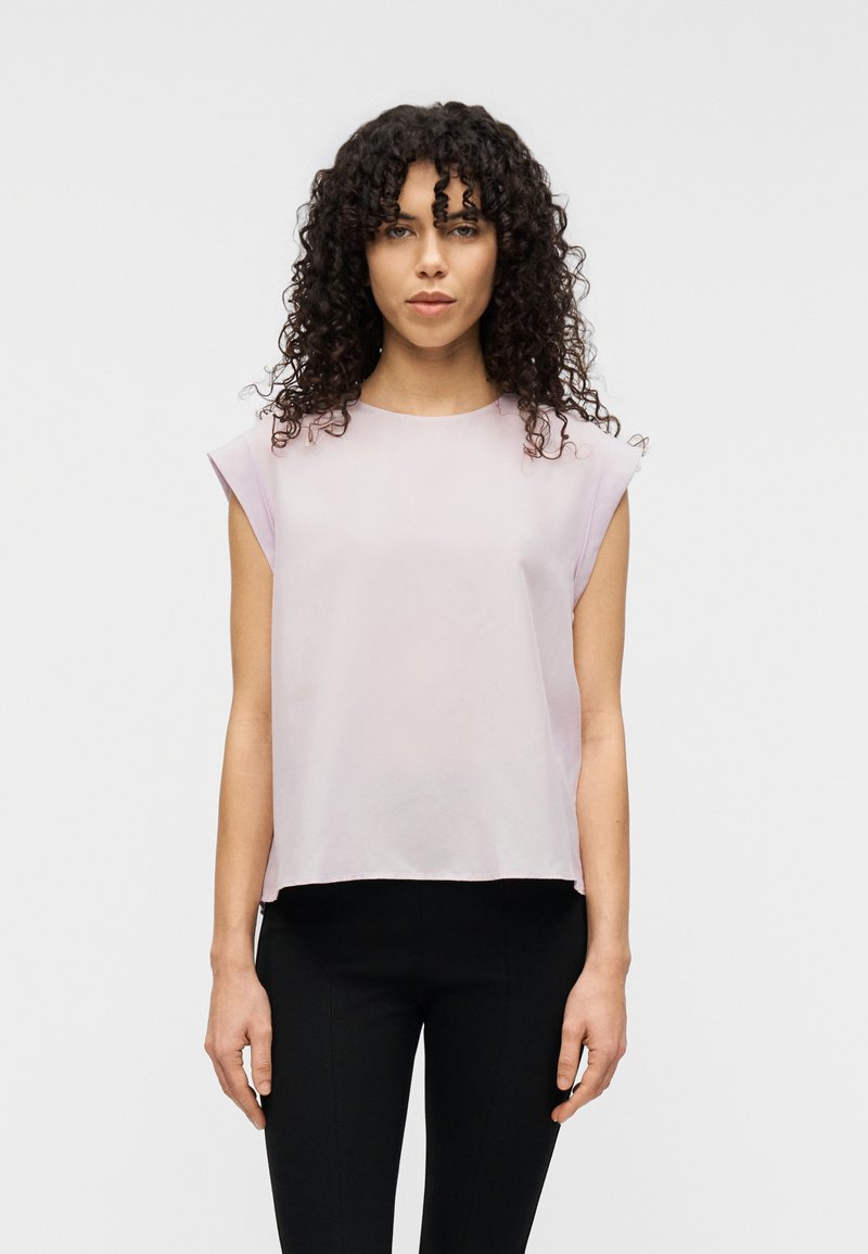 Ανοιχτό ροζ τοπ με κοντά μανίκια από απαλό ύφασμα, με στρογγυλή λαιμόκοψη και άνετη εφαρμογή, συνδυασμένο με μαύρο, εφαρμοστό παντελόνι.