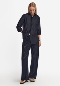 Mörkblå knäppt skjorta med krage och uppvikta ärmar, tillsammans med matchande vida byxor med en diamantmönstrad öppen väv.