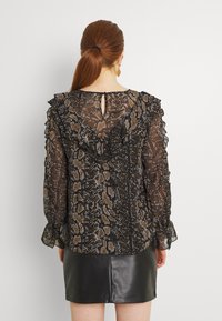 Blouse à imprimé animal noir et beige avec des accents froncés, des manches longues en voile et un détail en forme de trou de serrure à l'arrière. Associée à une jupe en cuir noire.