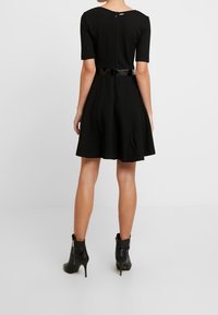 Svart kortärmad klänning med åtsittande överdel, utställd kjol och ett blankt svart bälte i midjan. Dragkedja bak. Bärs med svarta ankelboots.