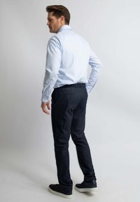 Lichtblauw longsleeve shirt gecombineerd met donkerdenim broek, beide met een slim fit. Sneakers zijn zwart met een witte zool.