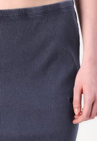 Marineblå ribbestrikket skjørt med en tettsittende design, elastisk livlinje og en liten logoakon i nærheten av kanten. Teksturen ser myk og elastisk ut.