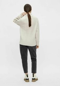 Pull en tricot de couleur crème avec des motifs texturés, associé à un pantalon gris foncé et des baskets imposantes blanches et noires. Vue arrière montrée.