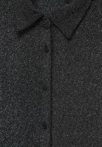 Chemise en tissu noir texturé avec de petites taches blanches, dotée d'un col et d'une rangée de boutons noirs au centre.