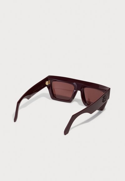 Lunettes de soleil bourgogne avec des verres carrés, une monture brillante et des branches élégantes et angulaires. Présente un logo sur le côté et des verres teintés foncés.