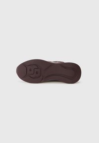 Sole di una sneaker marrone con motivo in rilievo e iniziali "BB" su uno sfondo bianco puro.