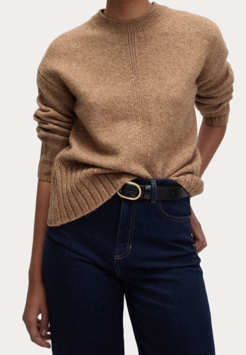 Brązowy sweter dzianinowy z okrągłym dekoltem i podwiniętymi rękawami, w połączeniu z ciemnoniebieskimi dżinsami i czarnym paskiem z złotą klamrą.