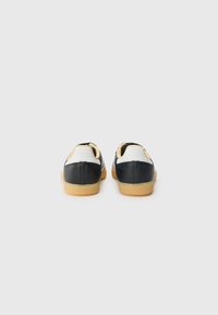 Svarta och vita sneakers med en slät läderutsida, vadderad häl, gummigummisulor och minimalistisk design. Bakifrån visas sömnadsdetaljer.