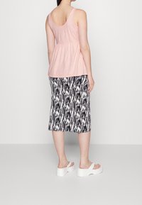 Ljusrosa ärmlös topp med ihopdragen midja, matchad med en svart- och vitmönstrad midi-skirt och vita klack sandsaler.