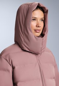 Ružičasta podstavljena jakna s visokim, strukturiranim kapuljačom i prošivenom teksturom, središnjim patentnim zatvaračem i glatkim završetkom.