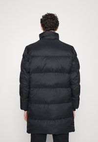 Chaqueta negra acolchada con cuello alto, diseño acanalado y mangas largas, hecha de un material suave y brillante.