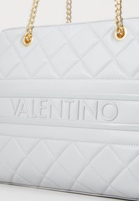 Quiltowany jasnoszary skórzany torebka na ramię z wytłoczonym logo "VALENTINO", złotymi akcentami i podwójnymi łańcuszkami na ramię.