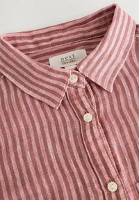 Chemise en lin rayée rose et blanche avec col et boutons blancs, affichant une étiquette "next 100% linen" à l’intérieur de l’encolure.