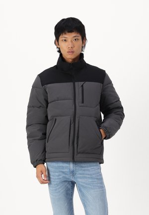 Padded jacket featuring a black upper section and dark gray lower section, with zippered pockets and elastic cuffs for a snug fit.