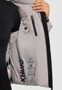 Lys grå vandtæt jakke indvendig med sorte detaljer, lynlåslomme og trykte plejeinstruktioner. Letvægts, vindmodstandsdygtigt design.