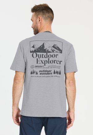 Mann trägt graues T-Shirt mit Berggrafik und Text „Outdoor Explorer“ sowie „outdoor wonders“ auf der Rückseite, steht vor weißem Hintergrund.