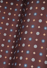 Brązowy materiał z kwiatowym wzorem z niebieskimi i białymi kwiatami, pomarańczowymi akcentami oraz małymi diamentowymi kształtami w całej powierzchni. Gładka tekstura.