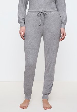 Grå sweatpants har en dragsko i midjan, avsmalnande ben och en mjuk textur. De är åtsittande vid anklarna med ribbade manschetter.