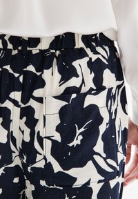 Blommönstrade byxor i marinblått och kräm, med elastisk midja och en bakficka, tillverkade av lätt tyg.