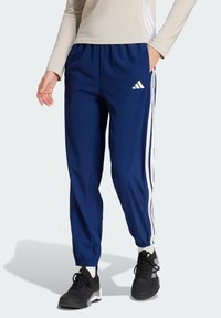 Tummansiniset urheiluhousut, joissa on valkoiset sivuviivat, elastinen vyötärö ja taskut. Vasemmassa reidessä on Adidas-logo.