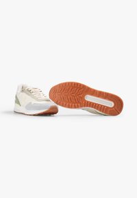 Zapatilla blanca y verde que presenta una mezcla de materiales de malla y ante. Suela de goma con textura antideslizante y detalle del logo visible en el lateral.