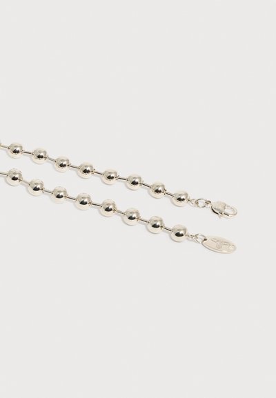 Βραχιόλι με αλυσίδα από μπίλιες σε ασημί τόνο με κούμπωμα σε σχήμα αστακού και οβάλ ταμπελάκι που φέρει χαραγμένο σύμβολο, τοποθετημένο σε απλό λευκό φόντο.