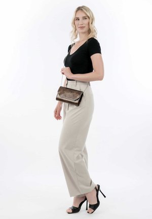 Top aderente nero, pantaloni beige a vita alta e tacchi neri aperti. Porta una pochette in bronzo con un design testurizzato e una tracolla.