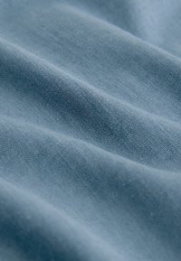 Tissu bleu doux à texture finement tricotée avec de légers plis créant des ombres et des reflets subtils.