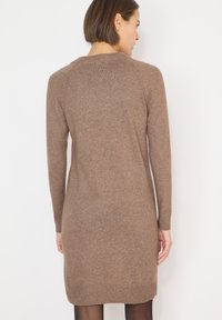 Bruine gebreide jurk met lange mouwen, geribbelde halslijn en manchetten, tot halverwege de dijen reikend, met een gladde textuur en een klassieke silhouet.