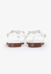 Witte platte sandalen met een strap-design, een bruine houten zool en metalen hardware-accenten. De banden zijn dun en verstelbaar.