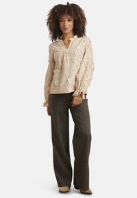 Light beige floral blouse with long sleeves, a v-neck, and ruffled cuffs, paired with wide-leg, black and white houndstooth patterned pants.