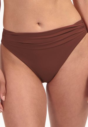 Slip bikini marrone arricciato indossato da una persona che mostra la zona addominale e la parte superiore delle cosce con le mani ai lati.