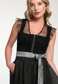 Schwarzes Kleid mit einem strukturierten Oberteil, transparenten Puffärmeln mit Polka-Dots und einem silbernen Satin-Gürtel. Verfügt über einen Reißverschluss und einen gerafften Rock.
