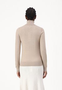 Beige rolák, fitted styl, dlouhé rukávy, ribbovaný vzor, měkký stretchový materiál, z pohledu zezadu, spárovaný s bílou pletenou sukní.