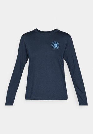 Pikkade varrukatega tumesinine T-särk, mis on valmistatud pehmest kangast. Omab ümmargust kaelust ja sinist ringikujulist logo vasakul rinnal.