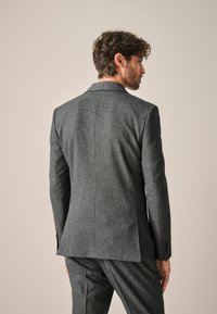 Chaqueta de traje ajustada para hombre en tejido texturizado gris oscuro. Cuenta con una abertura trasera, solapas de muesca y puños de tres botones.