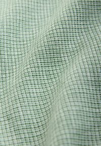 Zielony materiał w kratkę z fakturowaną powierzchnią, z drobnym wzorem kratki w jaśniejszych i ciemniejszych odcieniach zieleni.